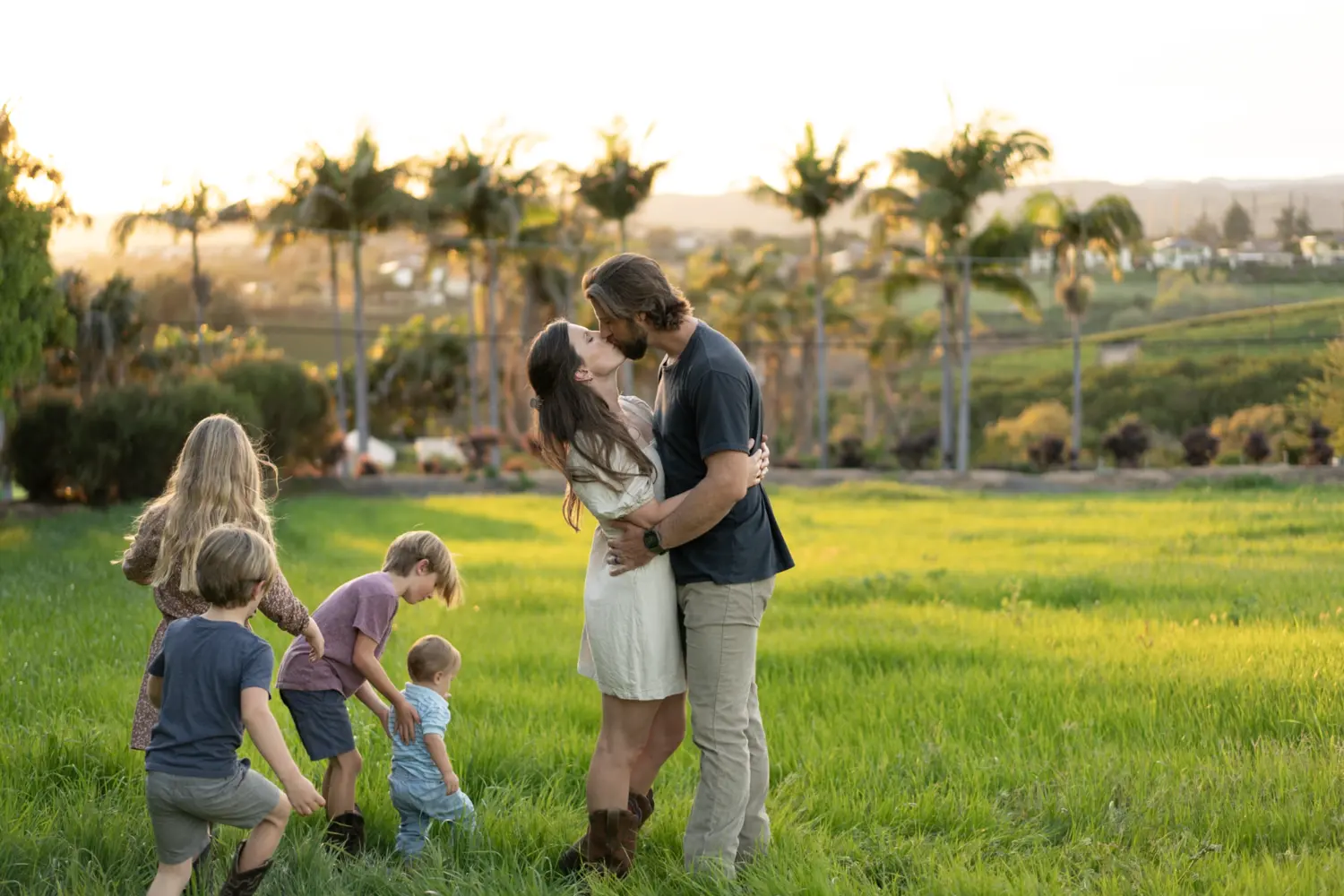 The parents share a kiss in a green field while their children play around them