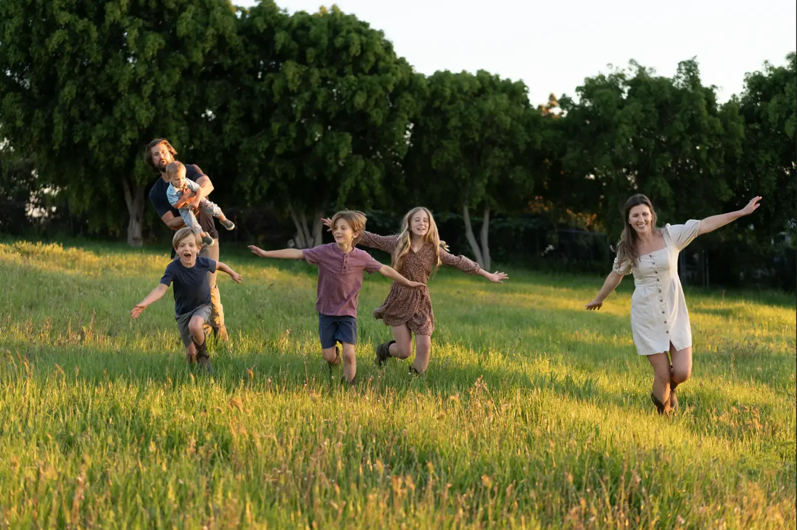 The children running through the tall grass toward the camera at golden hour