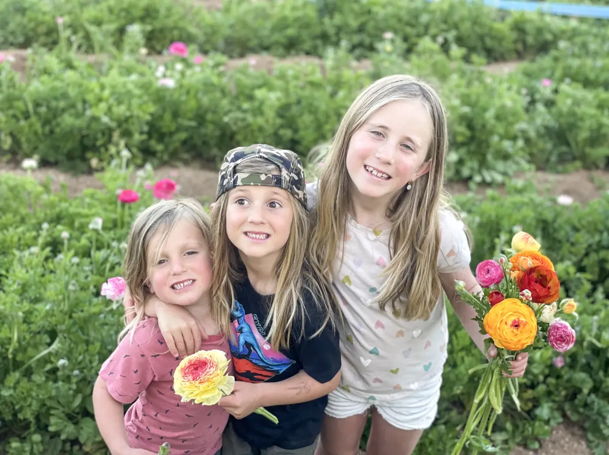 Three of the children holding cut ranunculus bouquets in the flower field