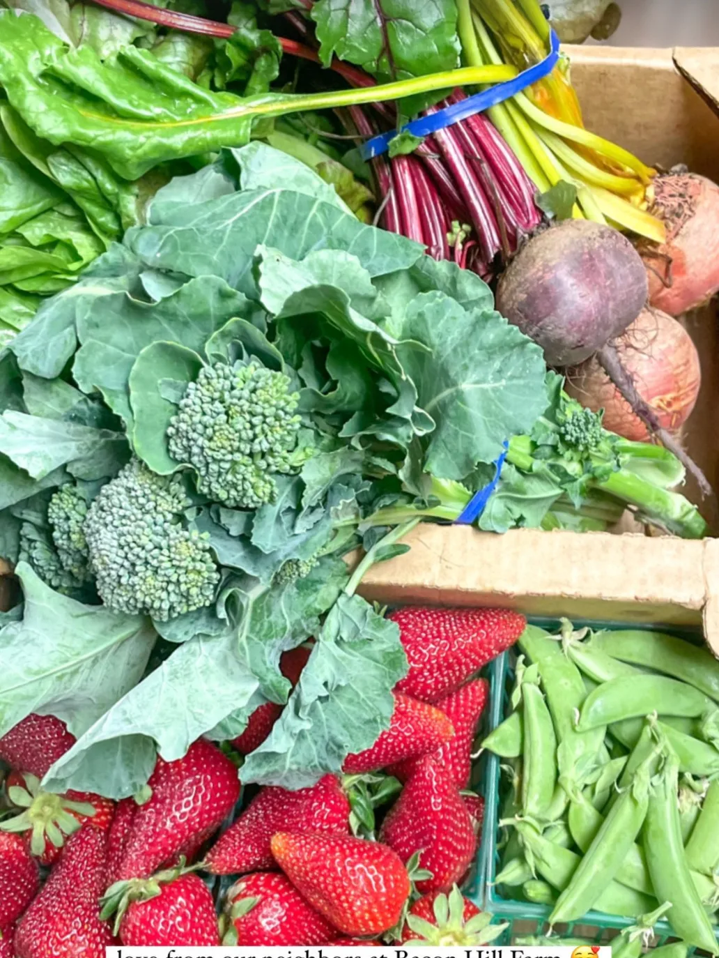 A crate of broccoli, greens, beets, strawberries and snap peas from the neighborhood harvest