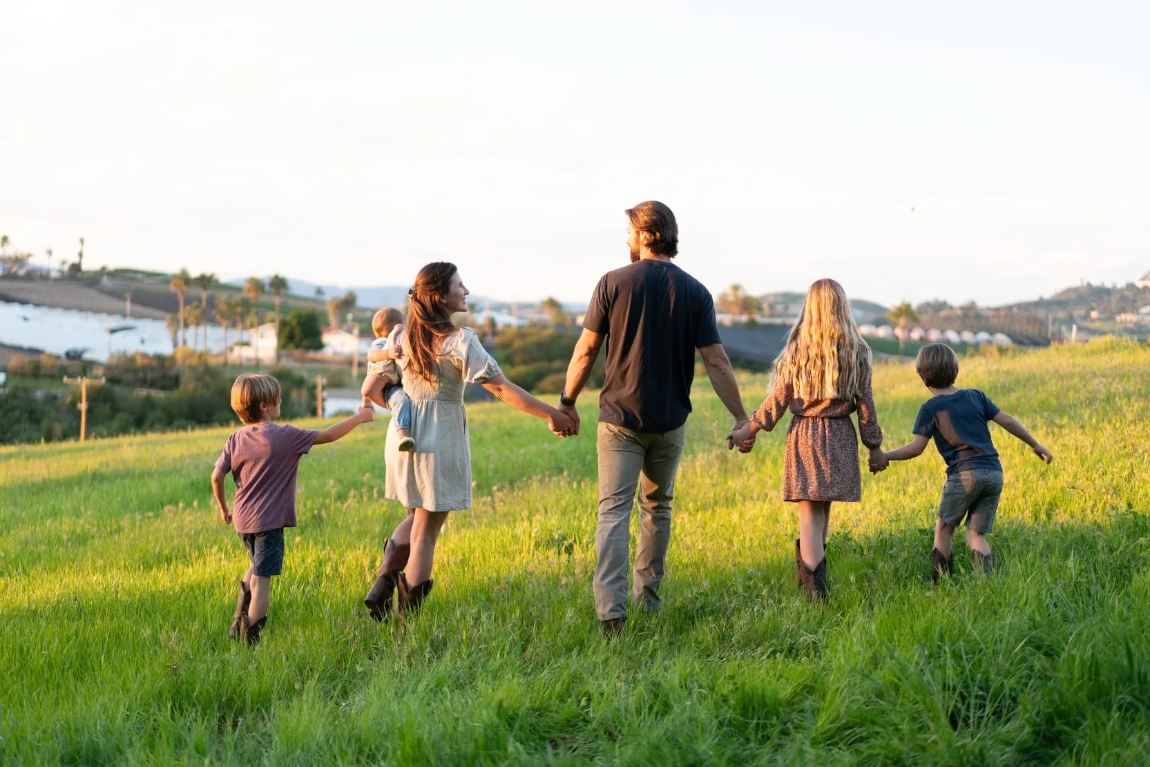 The Schleicher family walking hand in hand through the grass at Tradewinds Ranch at golden hour
