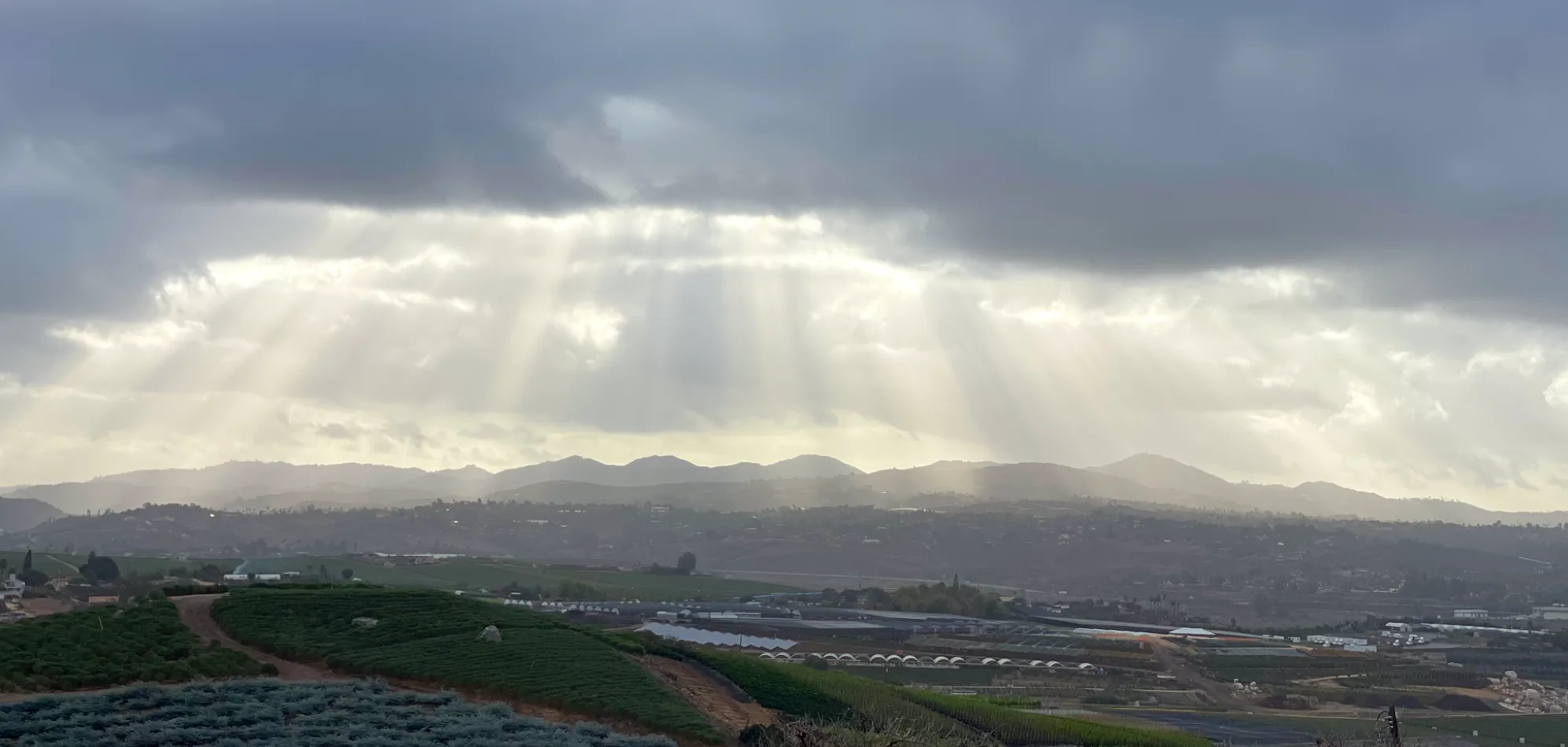 Light breaking through clouds over the farms and hills of North County San Diego, seen from the ranch