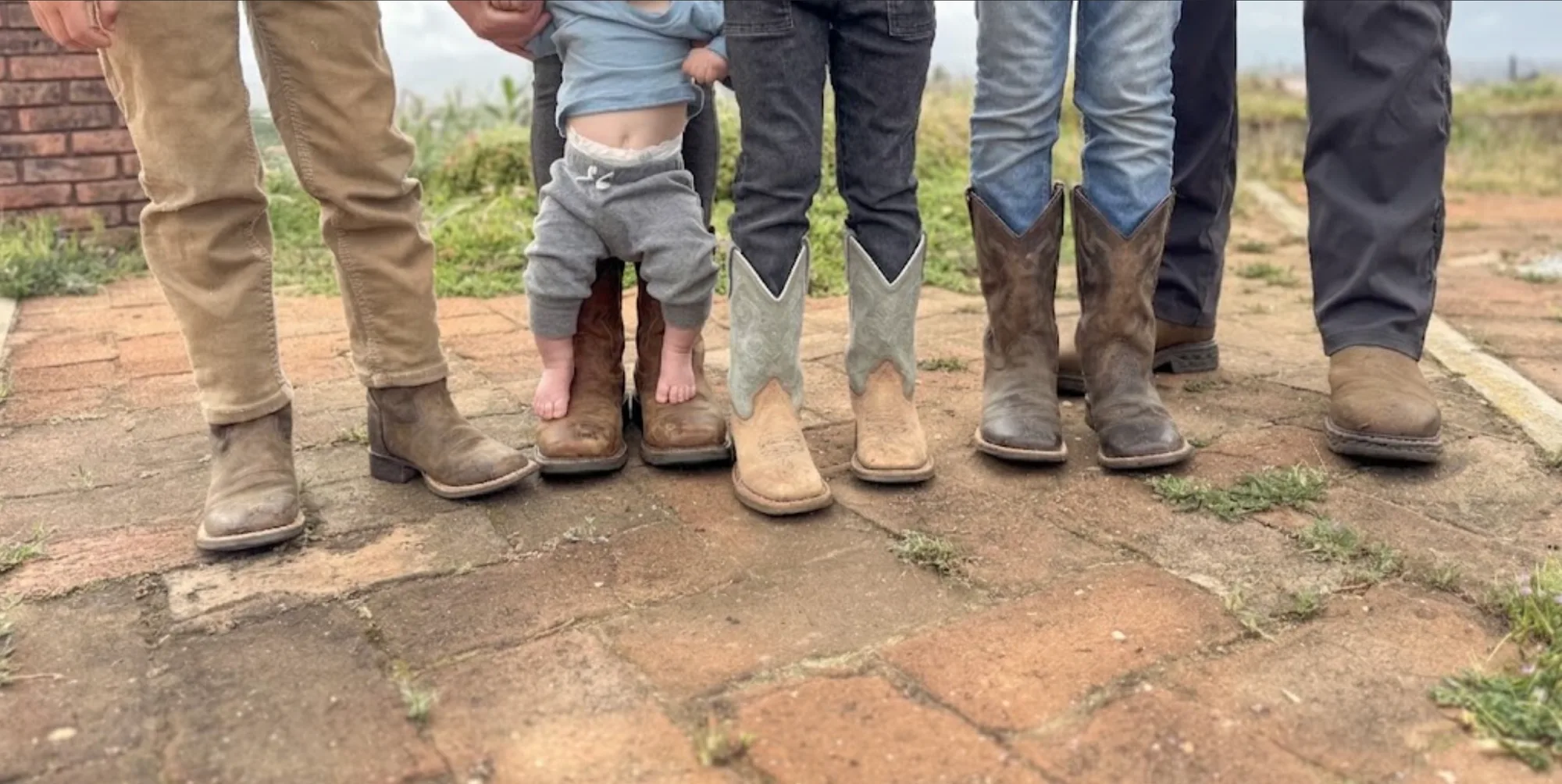 Boots of the whole family lined up on the old brick patio at Tradewinds Ranch, the baby standing barefoot on a pair