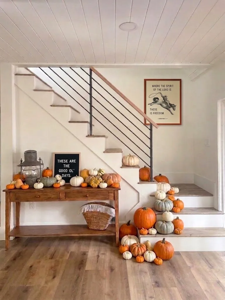 An indoor entry styled for fall, pumpkins massed along the staircase and across a wood console table