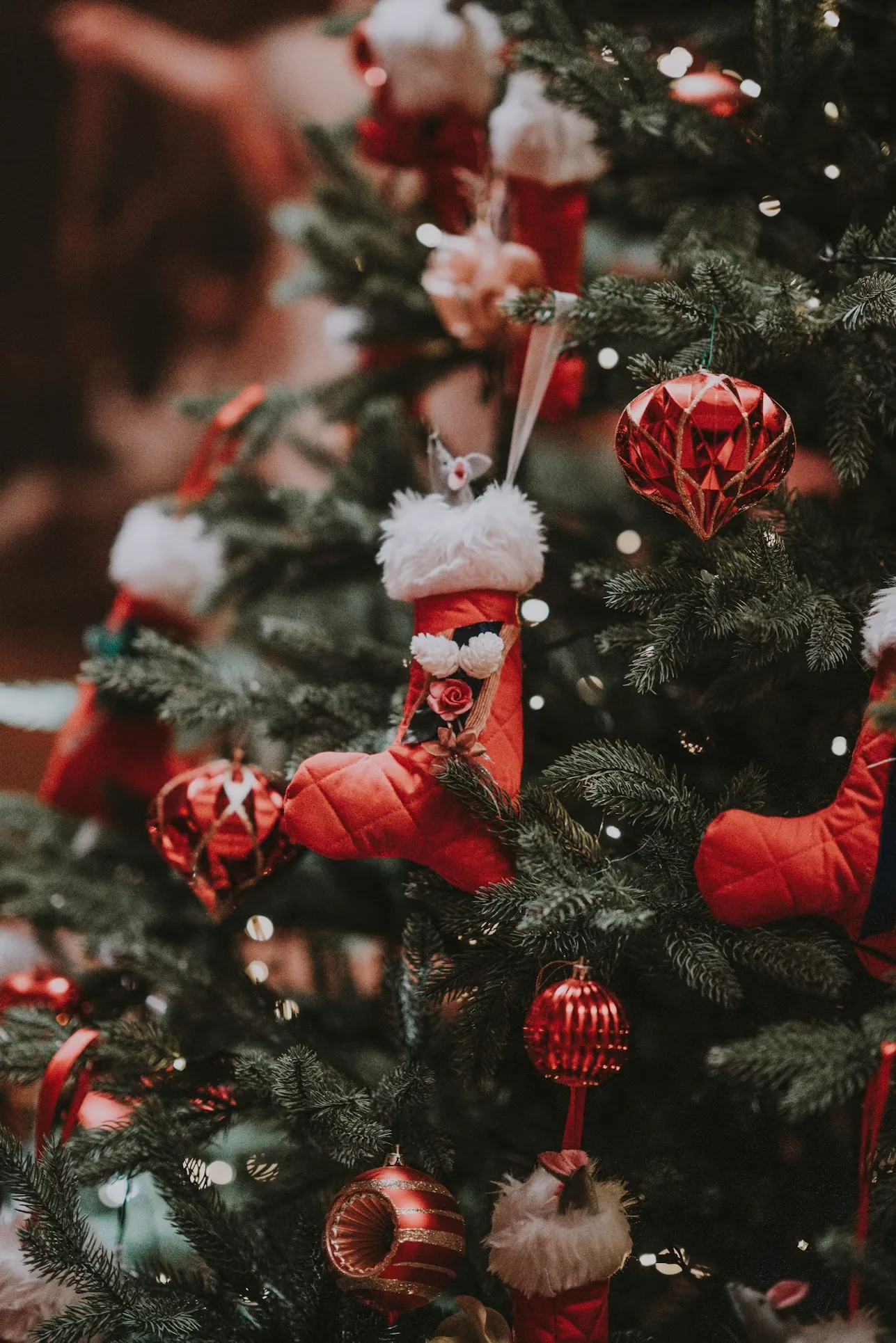 Red velvet stocking ornaments and glass baubles hung on a decorated tree