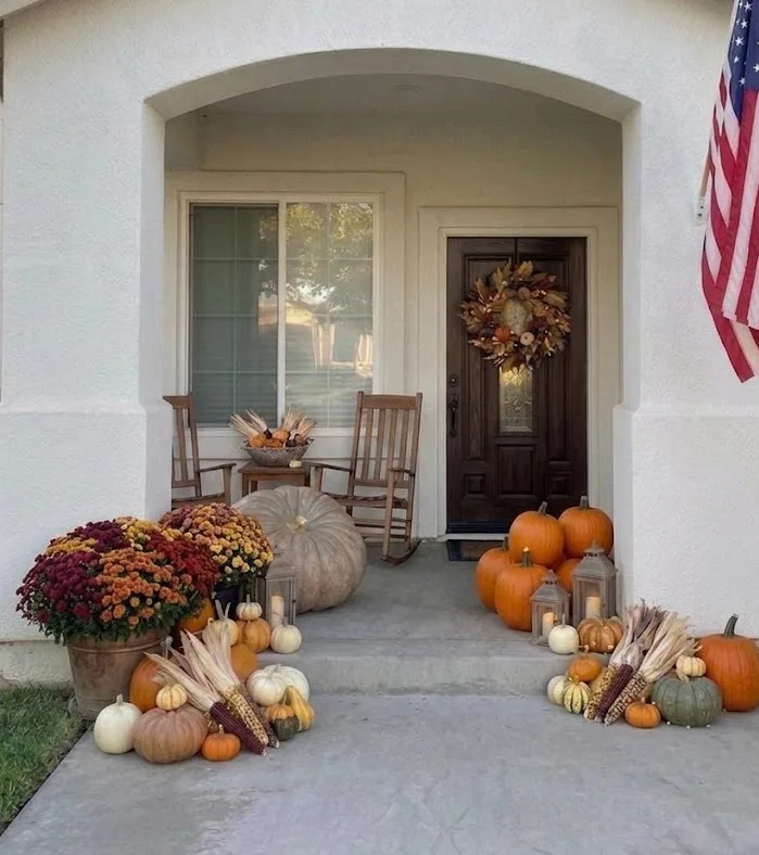 A styled fall porch with mums, cornstalks, and heirloom pumpkins flanking the door